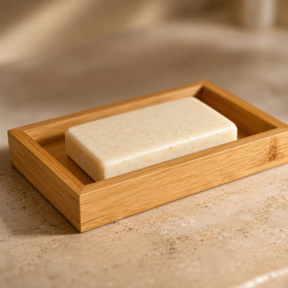 Bamboo soap dish detail close-up with natural cream soap bar on warm travertine bathroom surface, soft side light