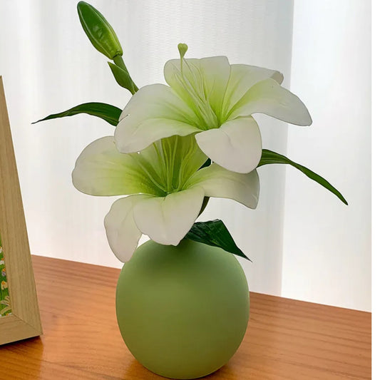Single faux lily stem in a small green ceramic vase beside a framed painting — Holm & Hearth