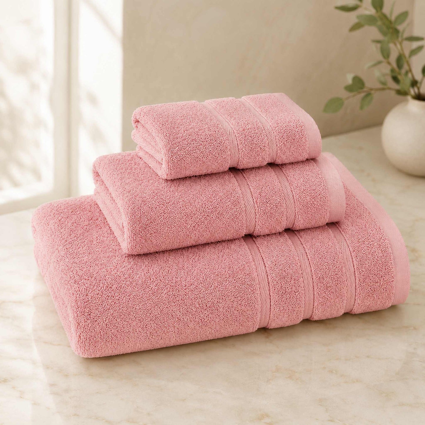 Pure cotton bath towel 3-piece set in blush with satin edge, folded on warm cream marble surface, soft natural light