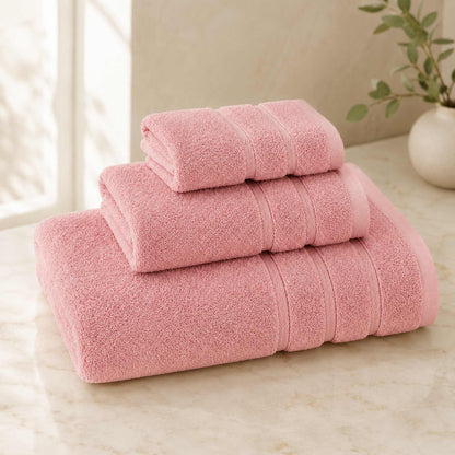 Pure cotton bath towel 3-piece set in blush with satin edge, folded on warm cream marble surface, soft natural light