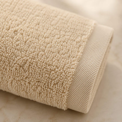Pure cotton bath towel detail close-up showing terry pile texture and satin border edge contrast, oat colourway