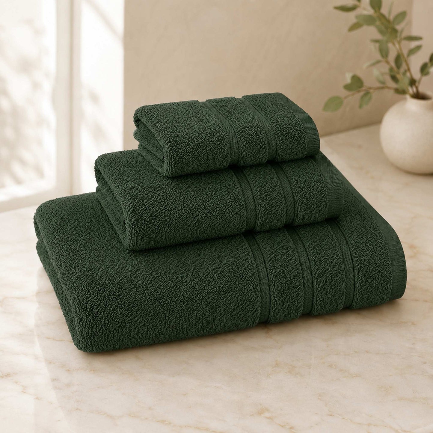 Pure cotton bath towel 3-piece set in forest with satin edge, folded on warm cream marble surface, soft natural light