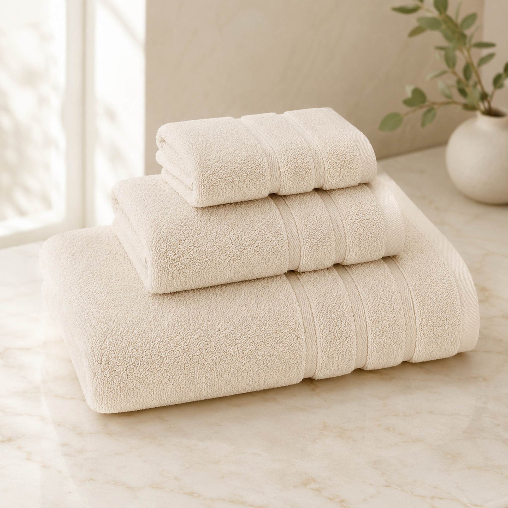 Pure cotton bath towel 3-piece set in ivory with satin edge, folded on warm cream marble surface, soft natural light