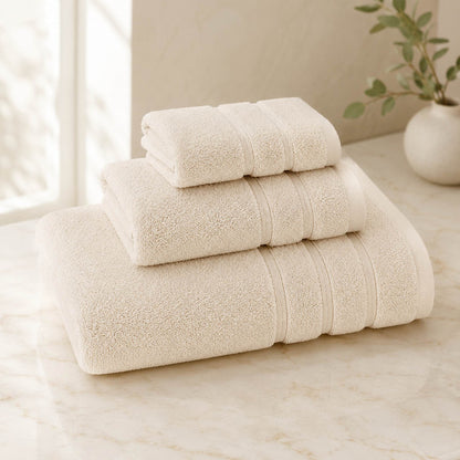 Pure cotton bath towel 3-piece set in ivory with satin edge, folded on warm cream marble surface, soft natural light