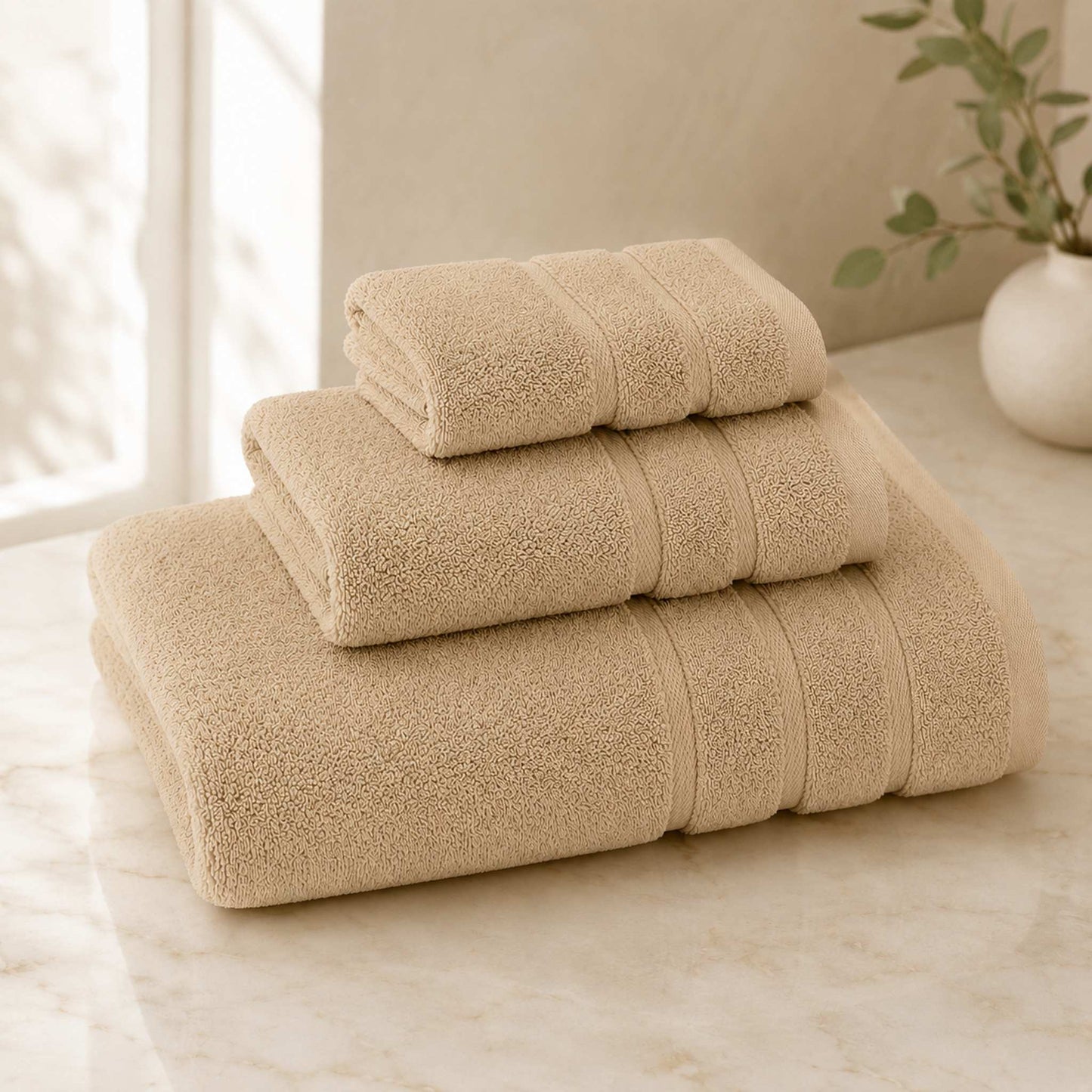 Pure cotton bath towel 3-piece set in oat with satin edge, folded on warm cream marble surface, soft natural light
