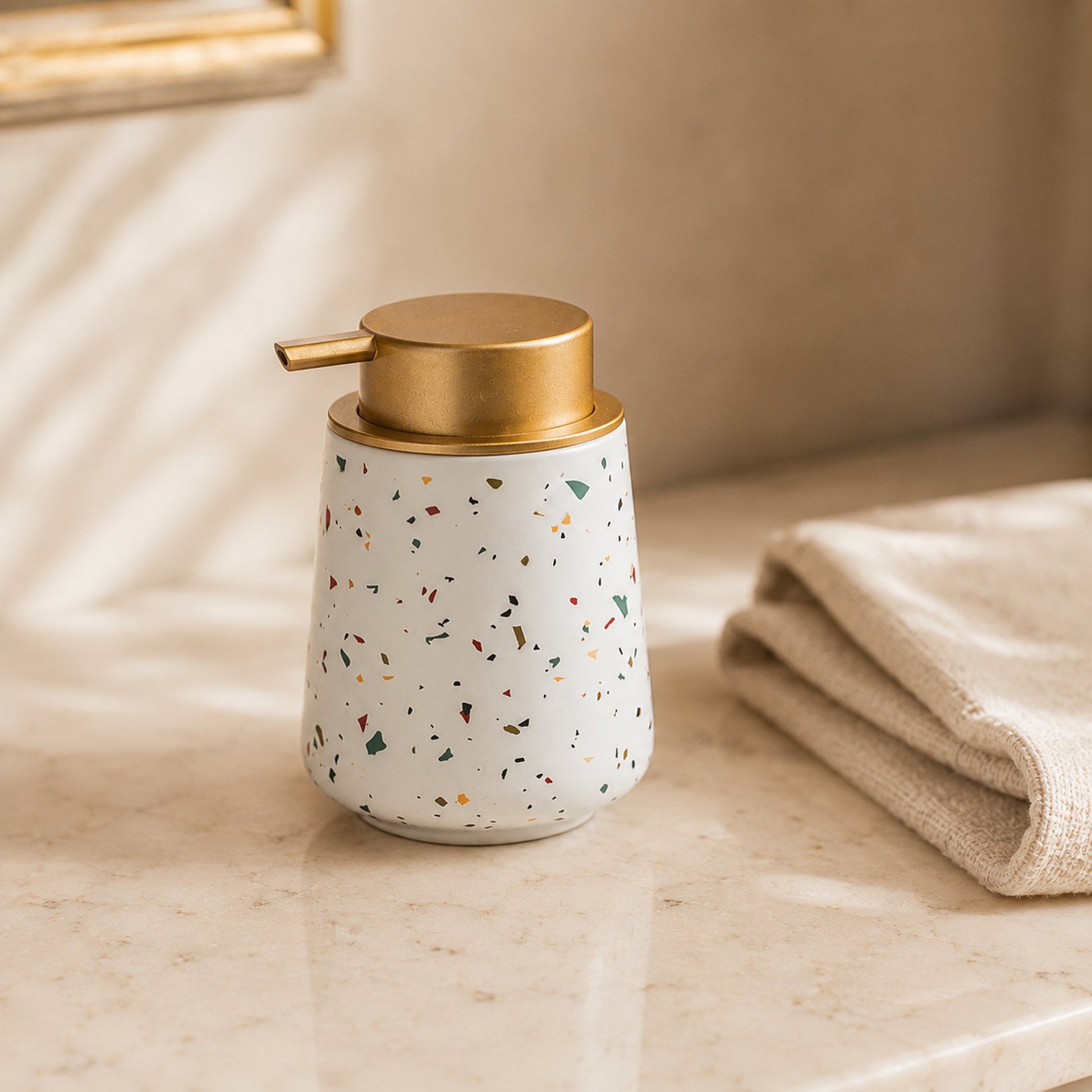 Conical terrazzo ceramic soap dispenser bottle with brushed brass pump on cream marble bathroom counter