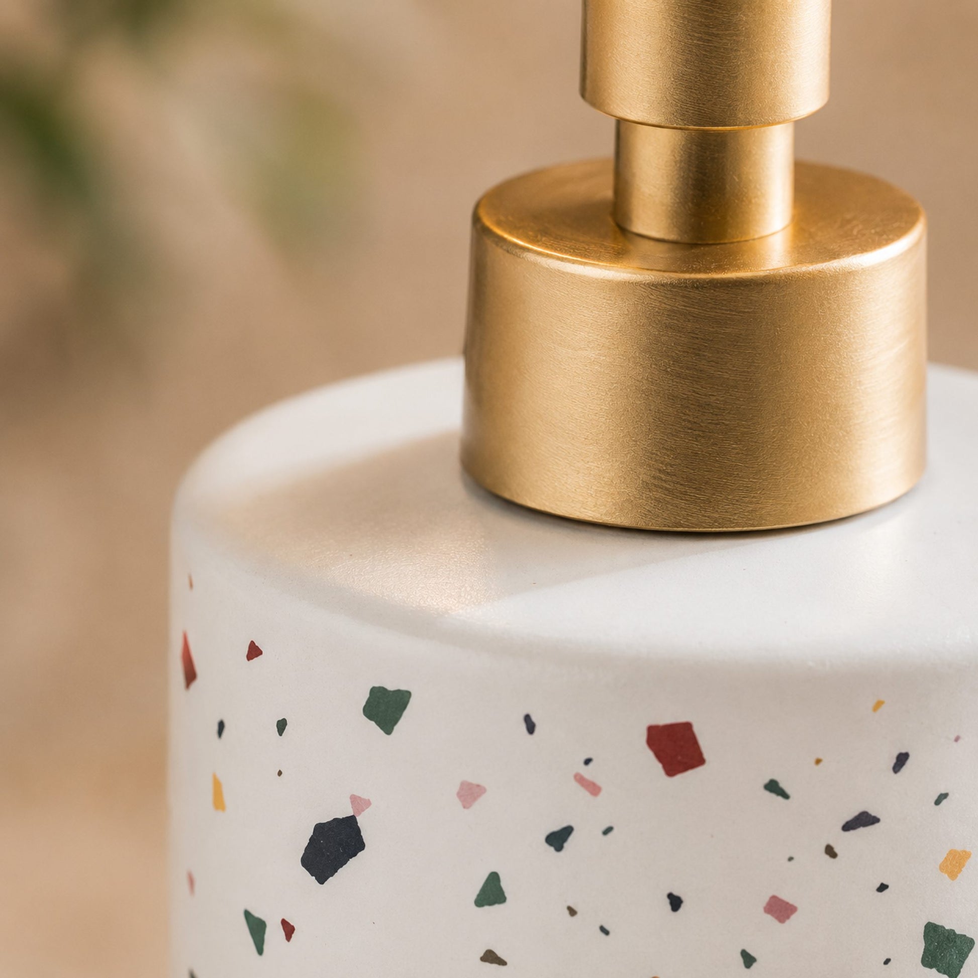 Close-up of brushed brass pump and terrazzo flecks on white ceramic soap dispenser bottle, glaze detail