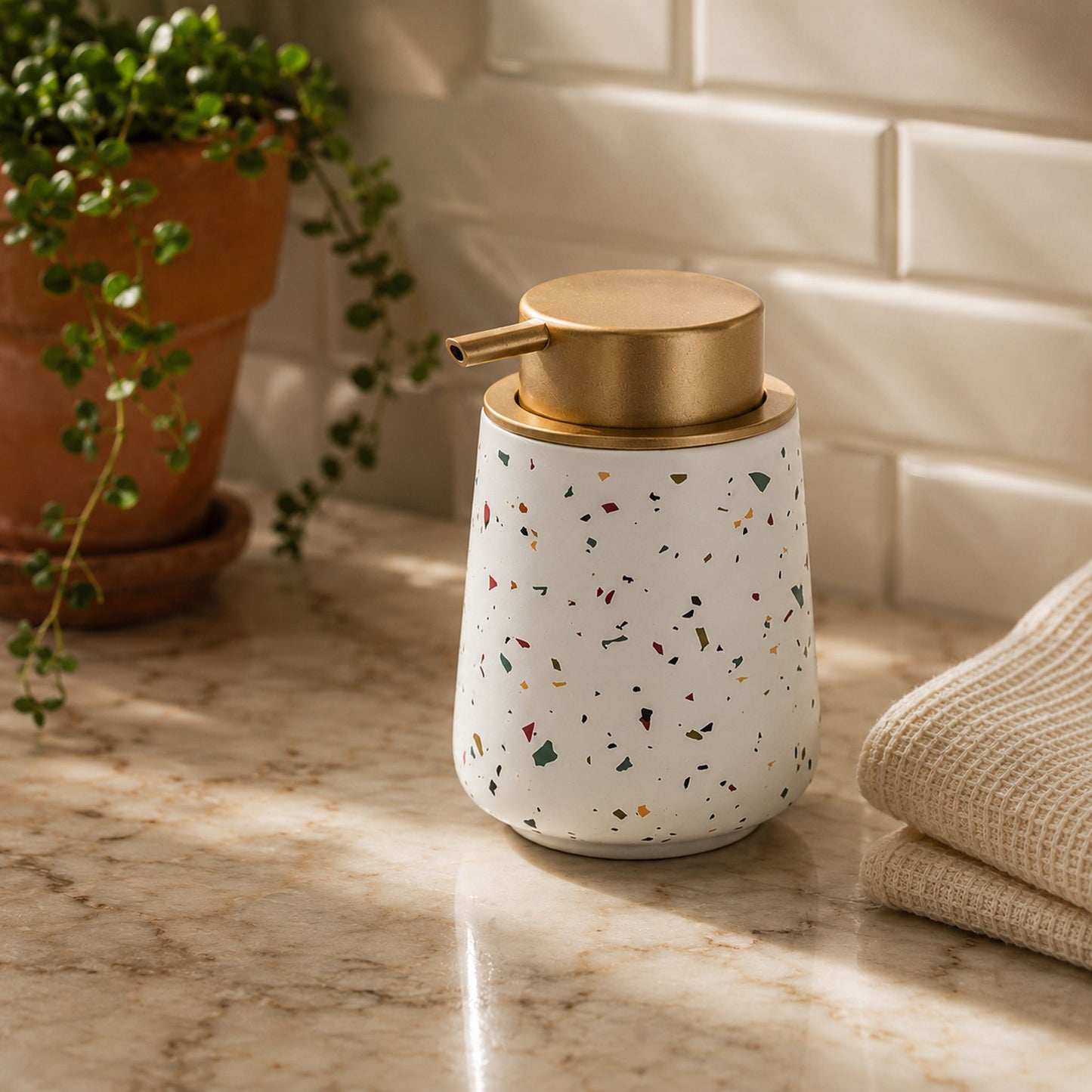 Conical terrazzo ceramic soap dispenser bottle styled on bathroom countertop with terracotta planter and waffle towel