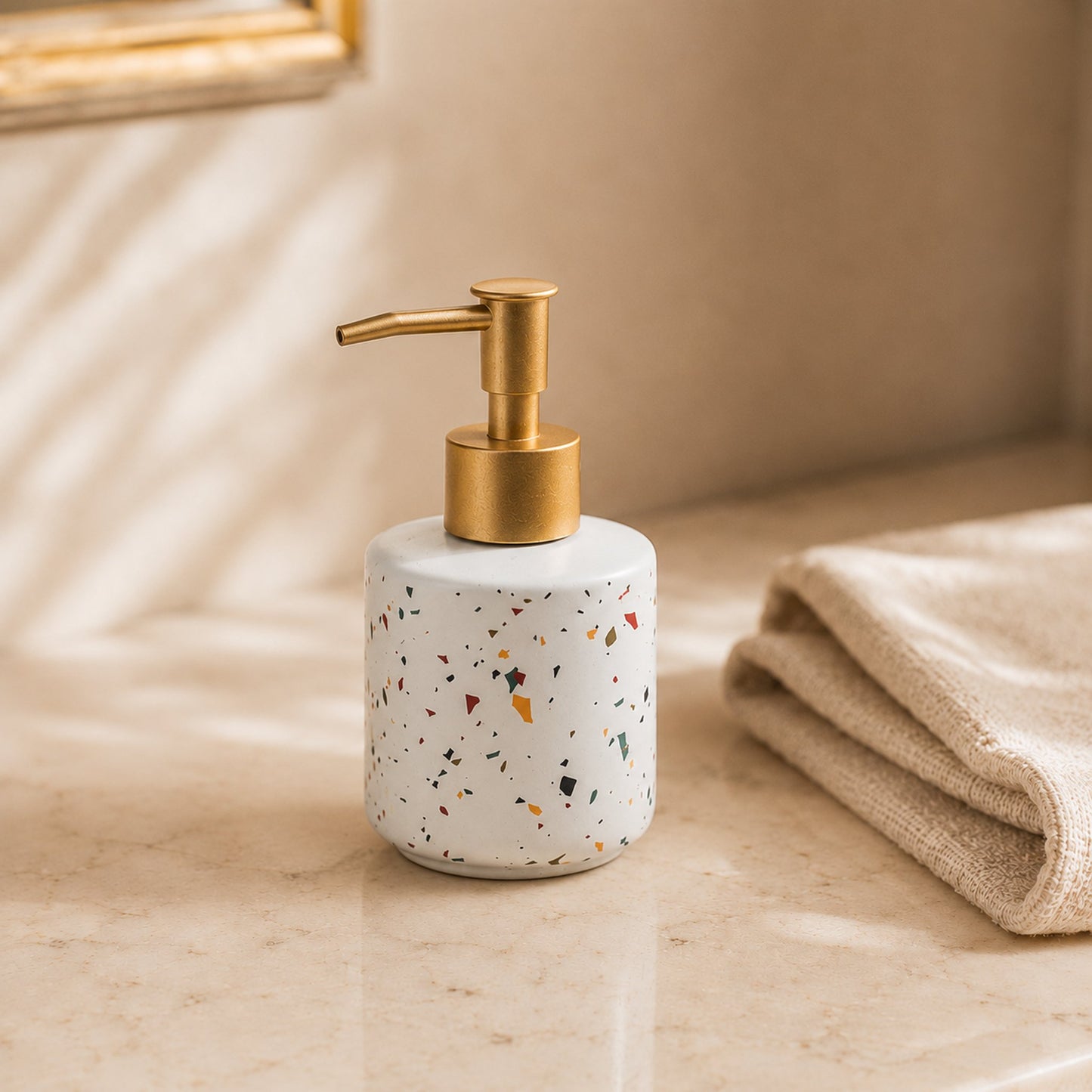 Round terrazzo ceramic soap dispenser bottle with brushed brass pump on cream marble bathroom counter