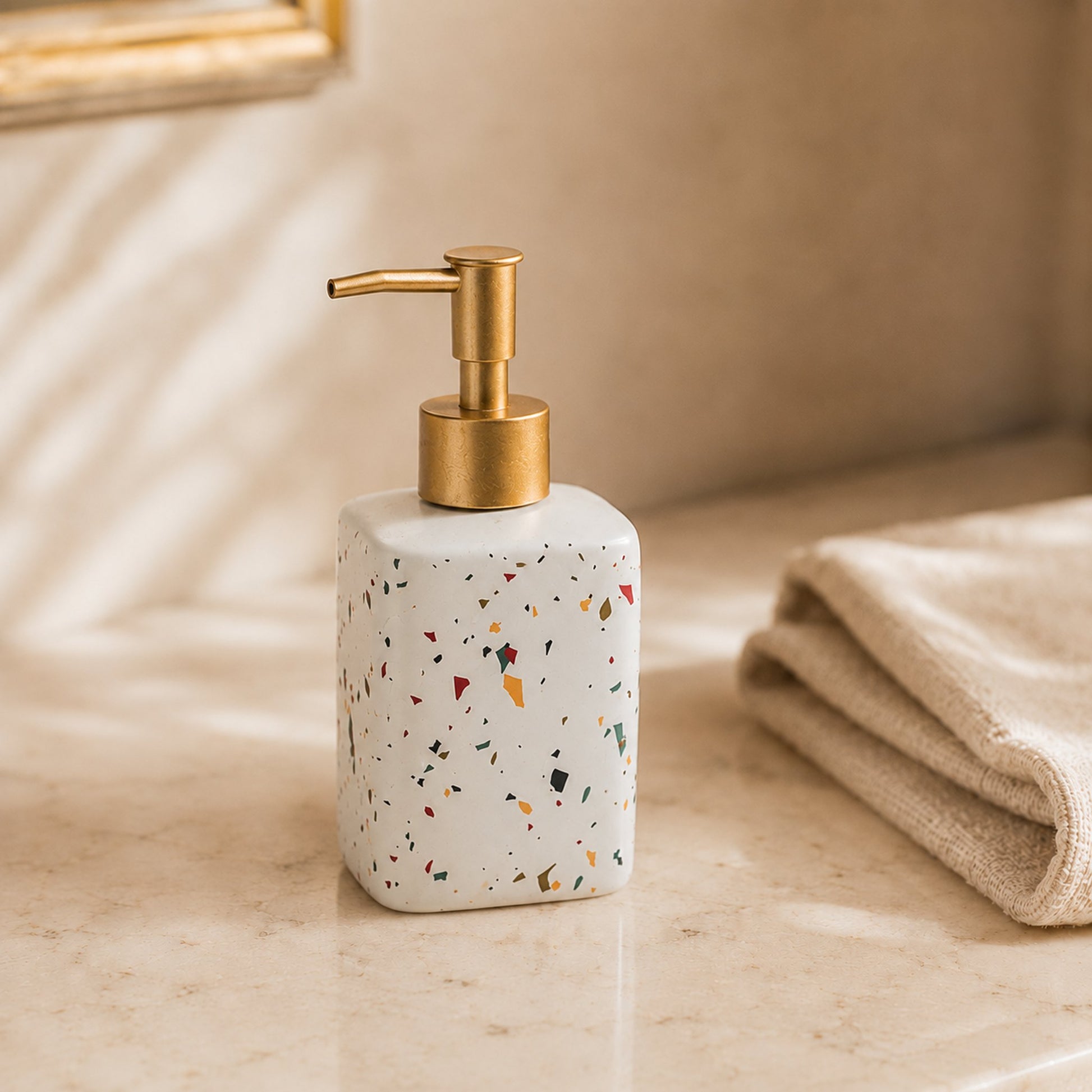 Square terrazzo ceramic soap dispenser bottle with brushed brass pump on cream marble bathroom counter