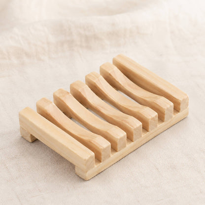 Natural wooden soap rack with drainage slats on cream linen surface, warm pale wood finish with visible grain