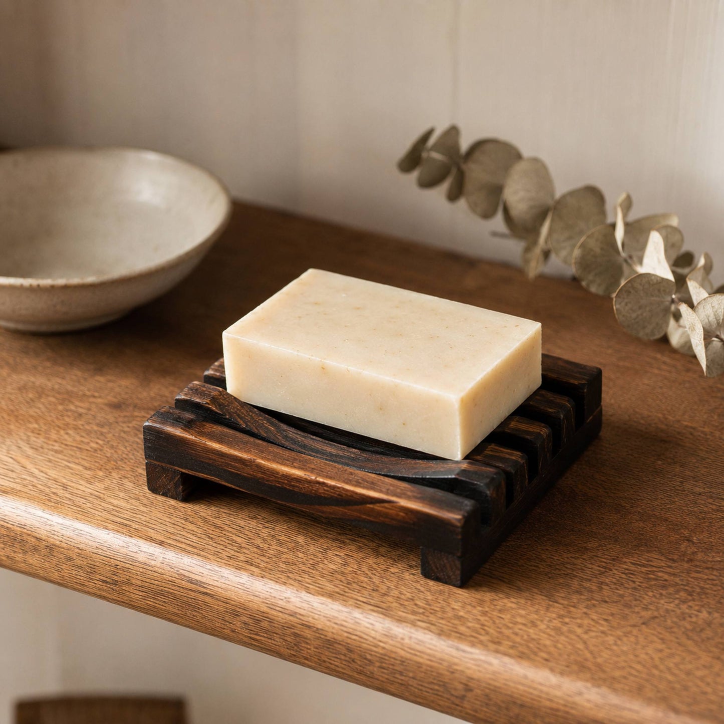 Charred wooden soap rack styled on warm oak bathroom shelf with ceramic dish and dried eucalyptus, lifestyle shot