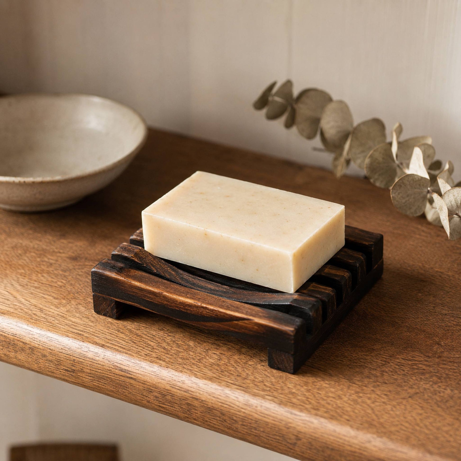 Charred wooden soap rack styled on warm oak bathroom shelf with ceramic dish and dried eucalyptus, lifestyle shot